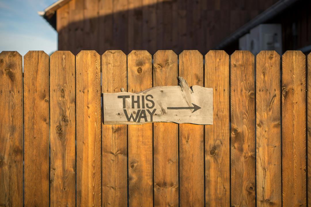 Une clôture en bois avec un une pancarte ou il y a écrit en anglais "de ce côté"